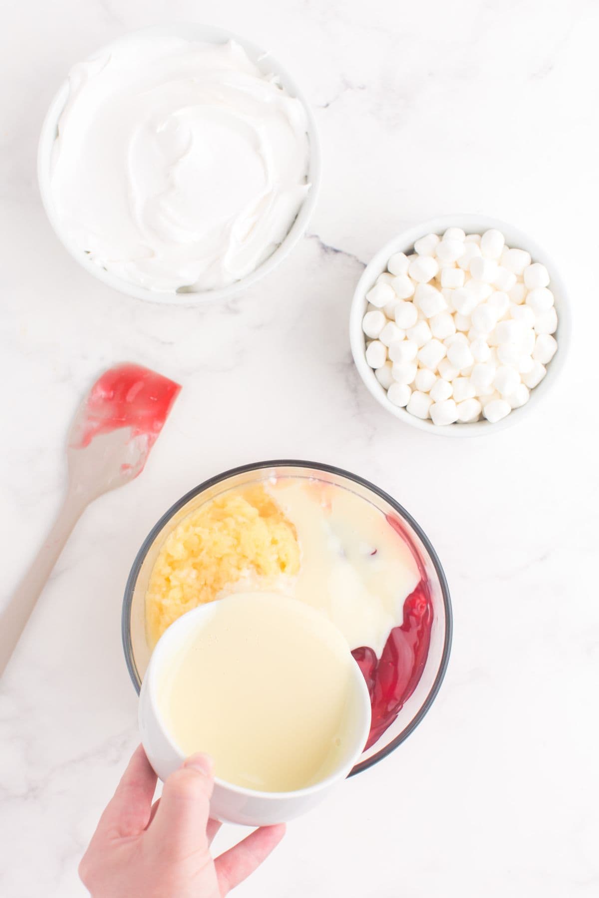 Cherry pie filling, pineapple, and condensed milk combined in glass bowl.