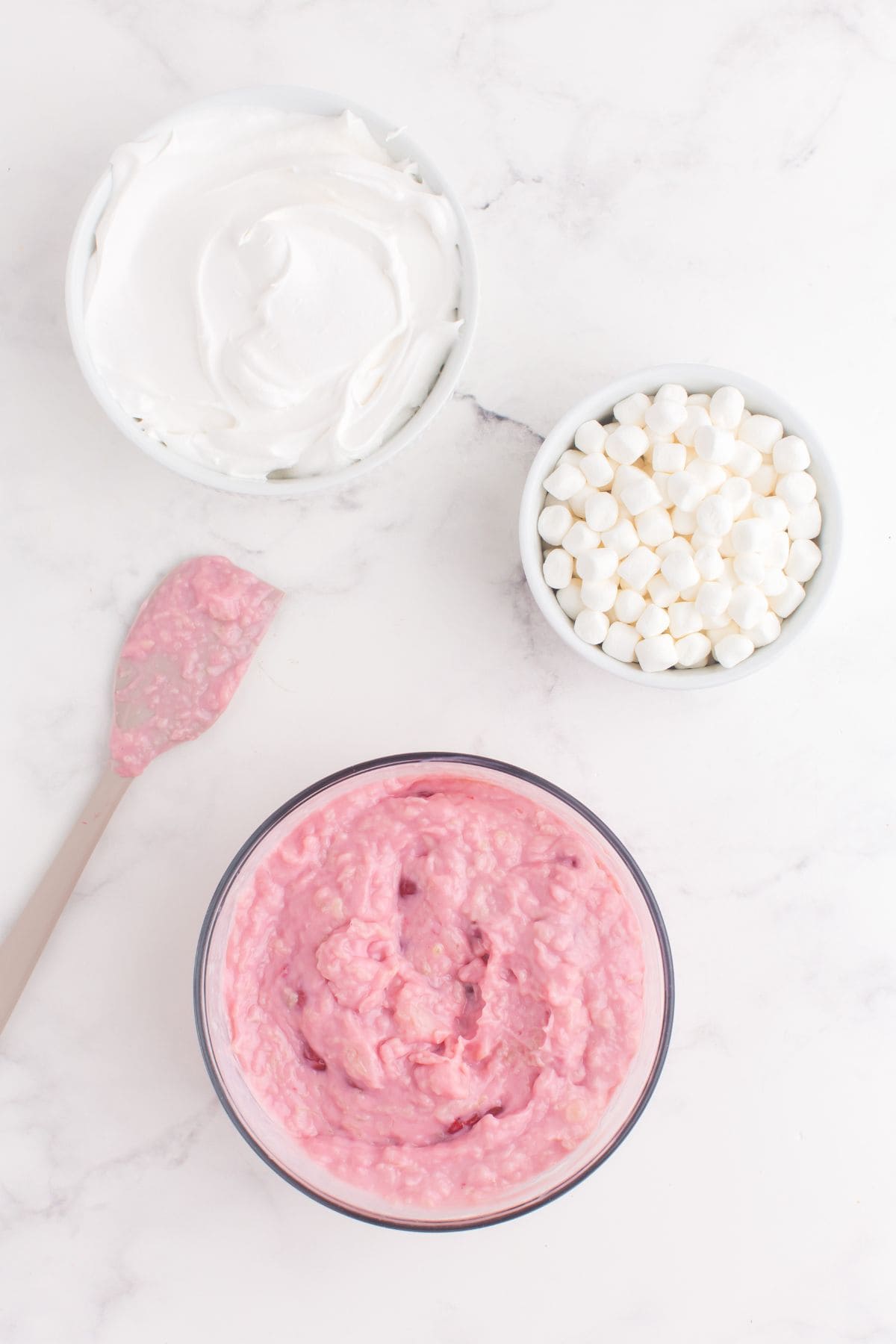 Cherry pie filling, pineapple, and condensed milk stirred together in a glass mixing bowl.