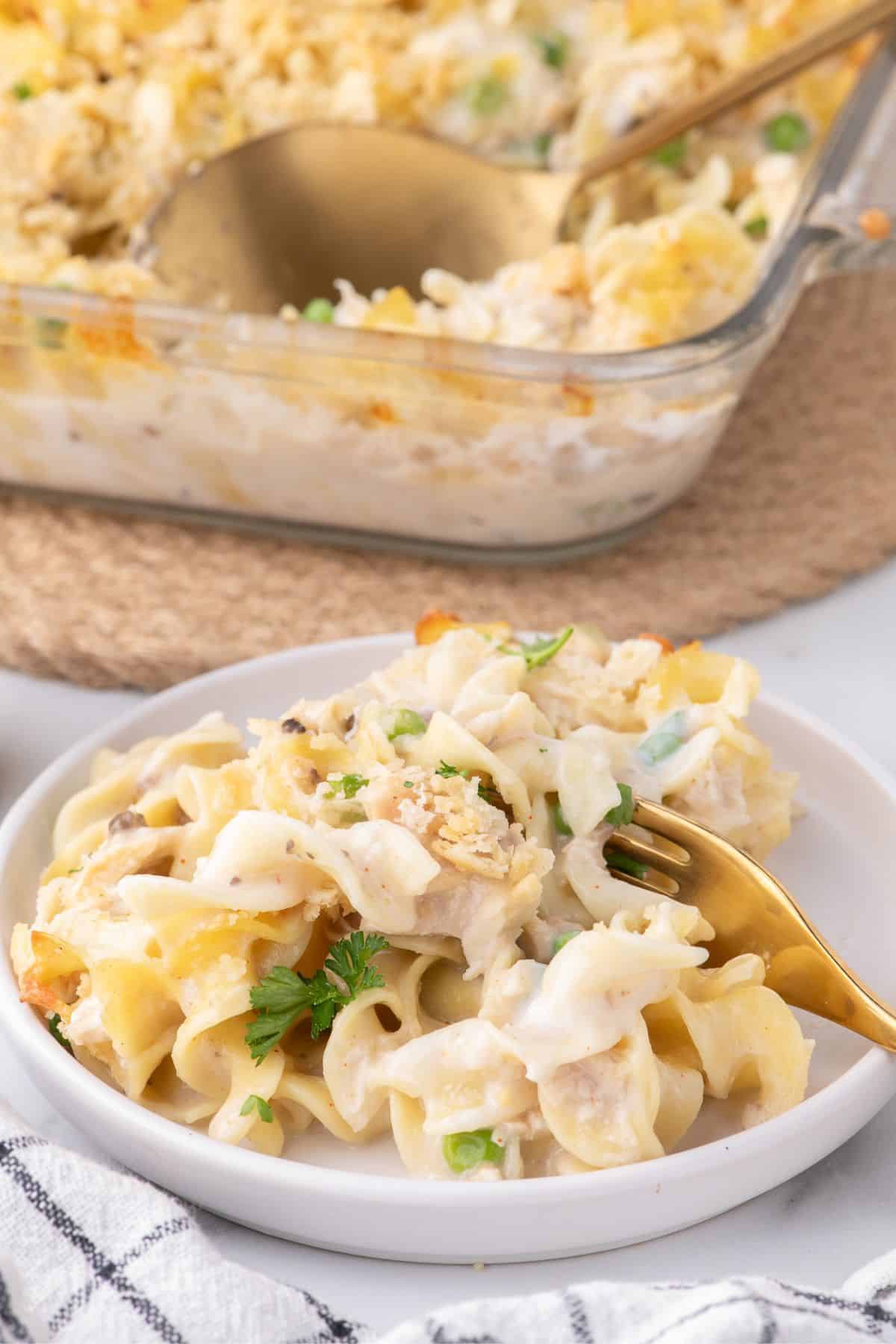 Easy tuna casserole on a white dinner plate. The glass baking dish with the casserole is set just behind the plate.