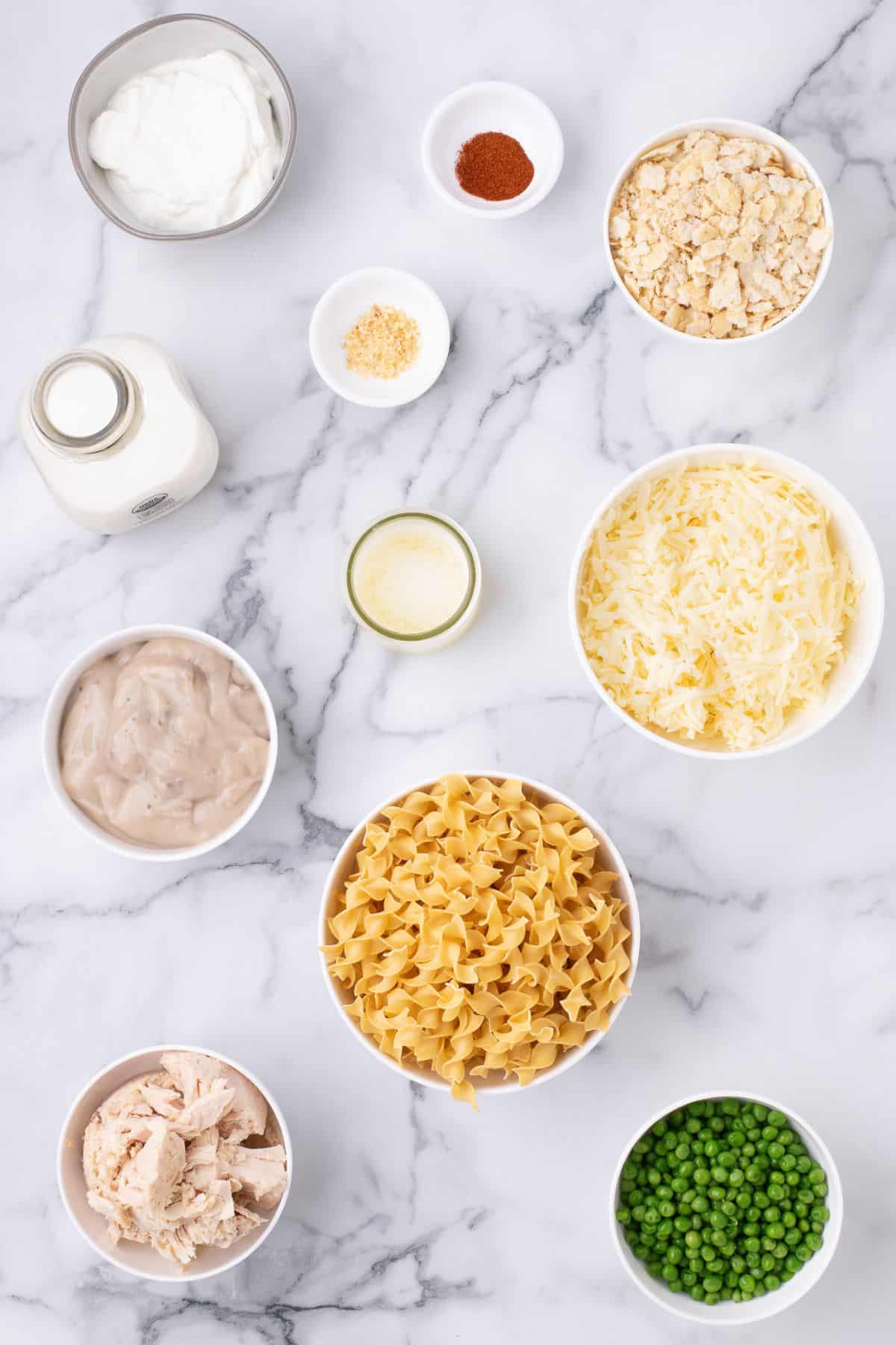 Ingredients for easy tuna casserole recipe: butter, salt, egg noodles, cream of mushroom soup, albacore tuna, sour cream, dried onion, cayenne pepper, cheddar cheese, frozen peas, milk, Ritz crackers, and fresh parsley.