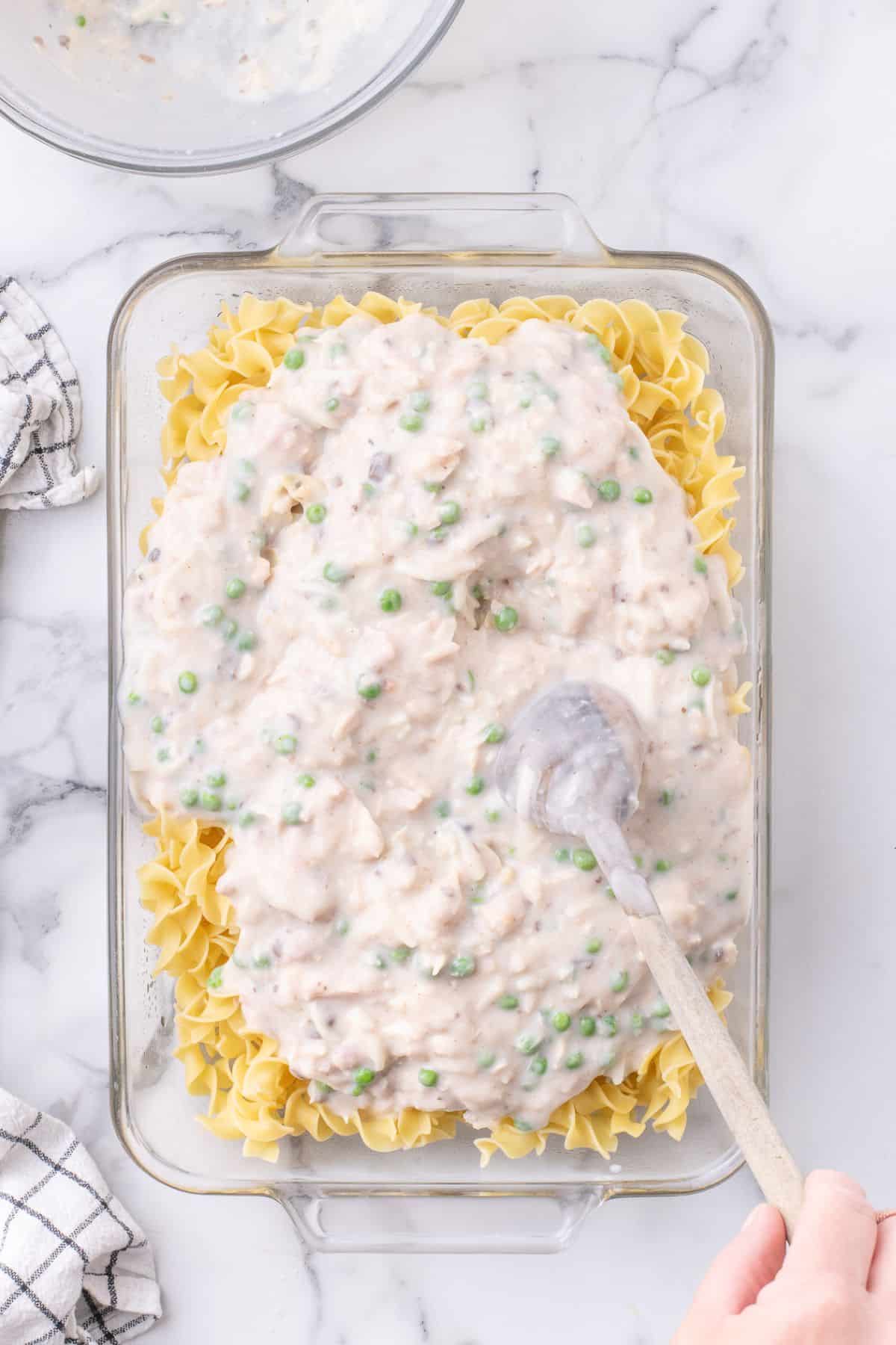 Cooked noodles and sauce combined in a glass mixing bowl.