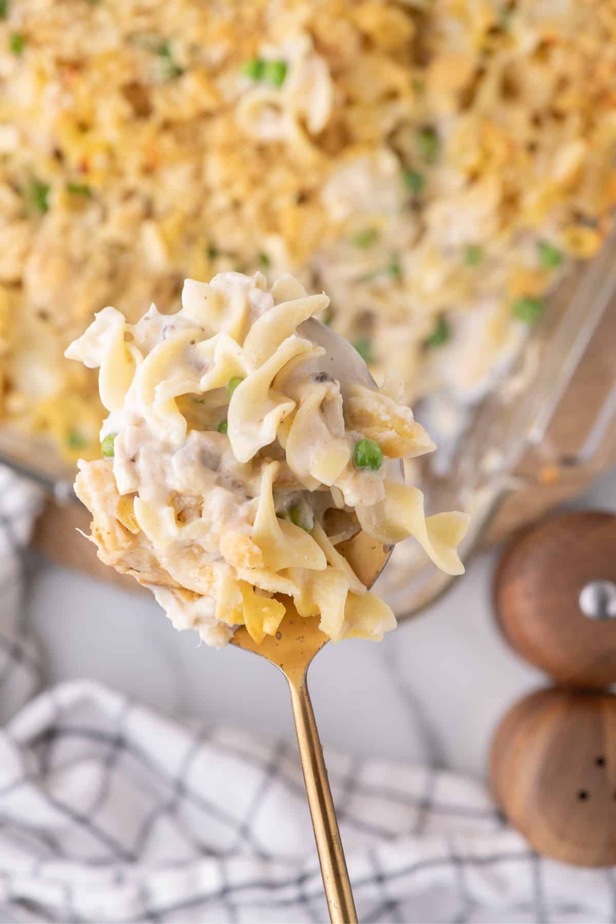 A serving spoon lifting a portion of tuna casserole out of a glass baking dish.