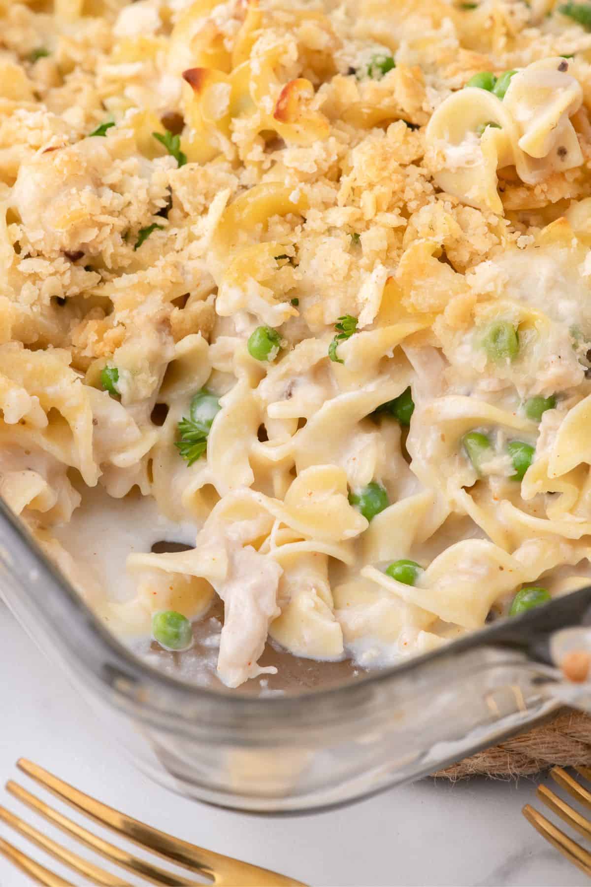 Tuna casserole in a glass baking dish. A serving has been removed from the corner of the baking pan.