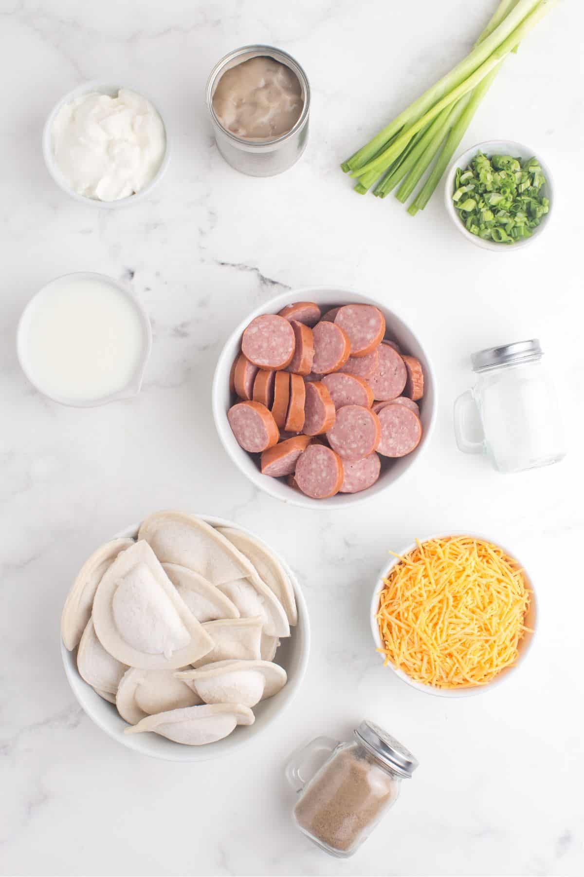 Ingredients for pierogi casserole: frozen pierogi, kielbasa, cream of mushroom soup, milk, sour cream, cheddar cheese, salt, pepper, and green onion.