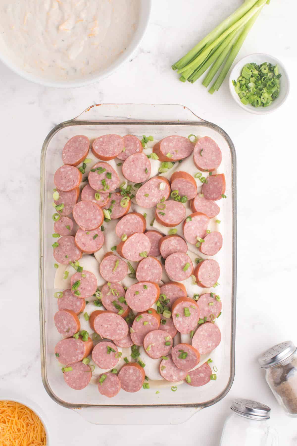 Sliced kielbasa and green onions layered on top of the pierogi layer.