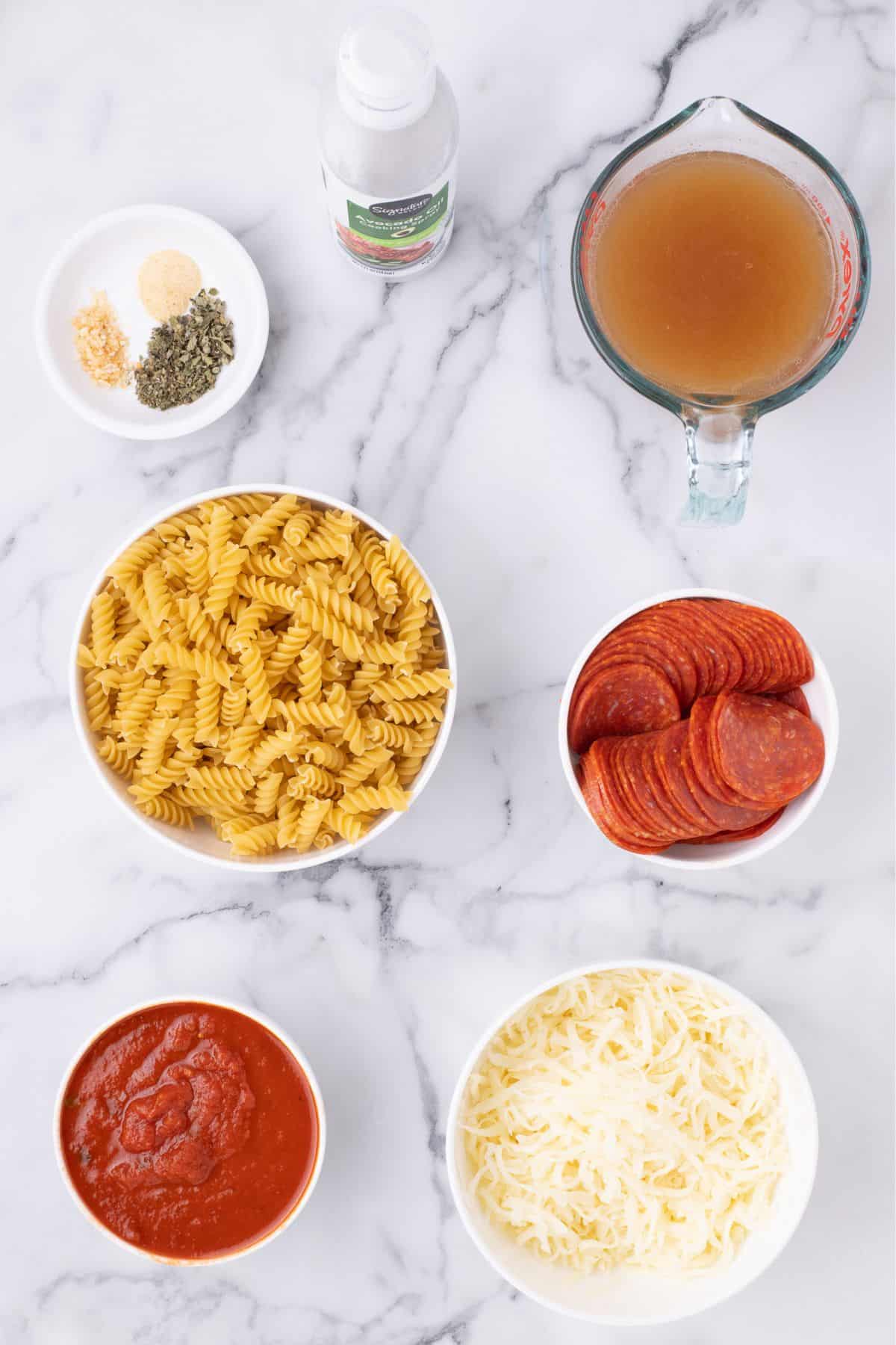 Ingredients for pizza casserole: rotini pasta, marinara pasta sauce, beef broth, dried minced onion, garlic powder, dried oregano, mozzarella cheese, and pepperoni slices.