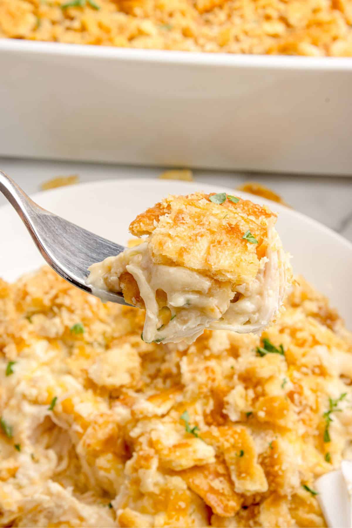 Ritz chicken casserole on a white dinner plate. A fork is lifting a bite above the plate.