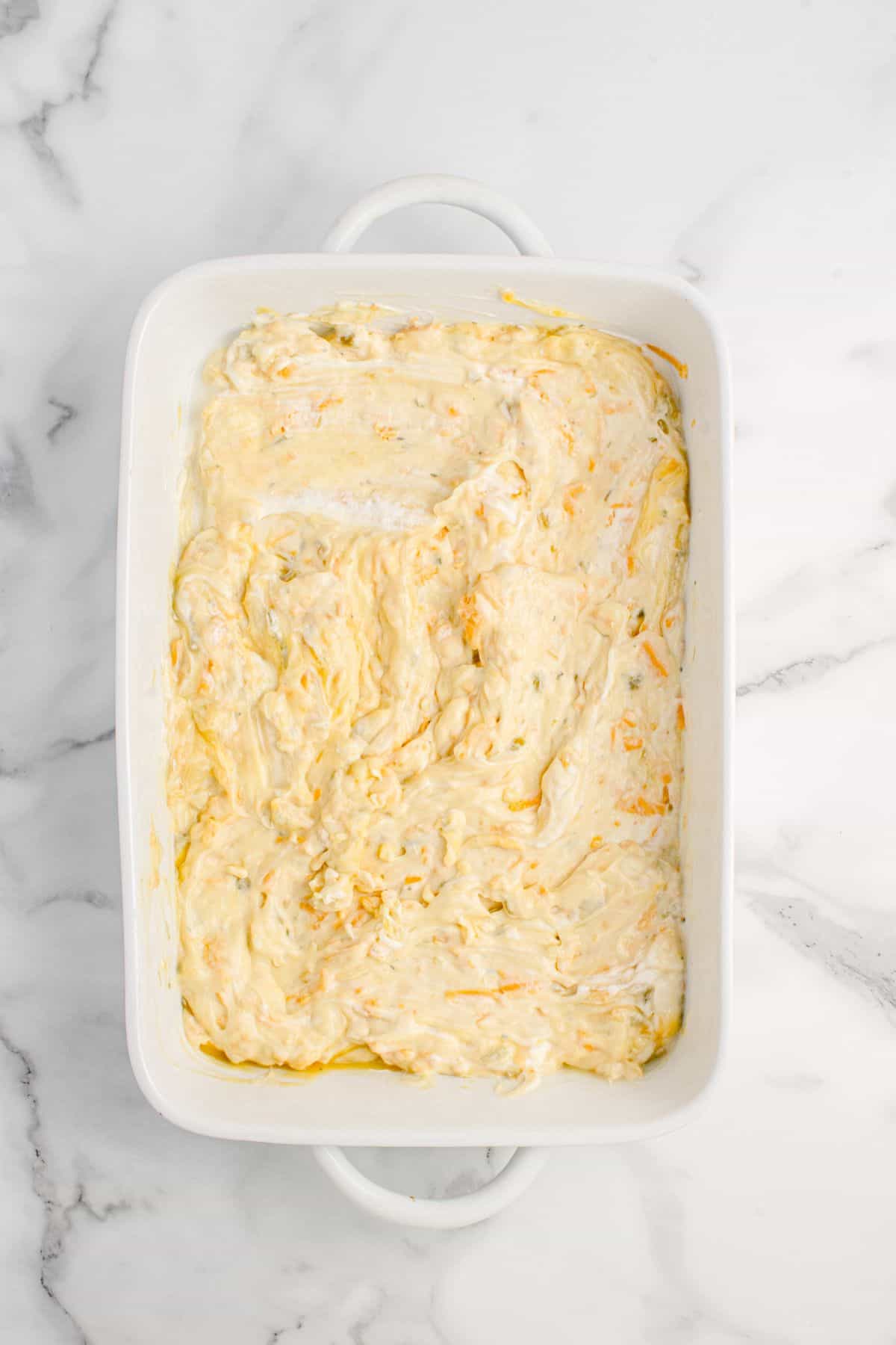 The rotisserie chicken, chicken soup, celery soup, sour cream, milk, ranch seasoning, and half the cheddar cheese mixed together in a baking dish ready to be baked.