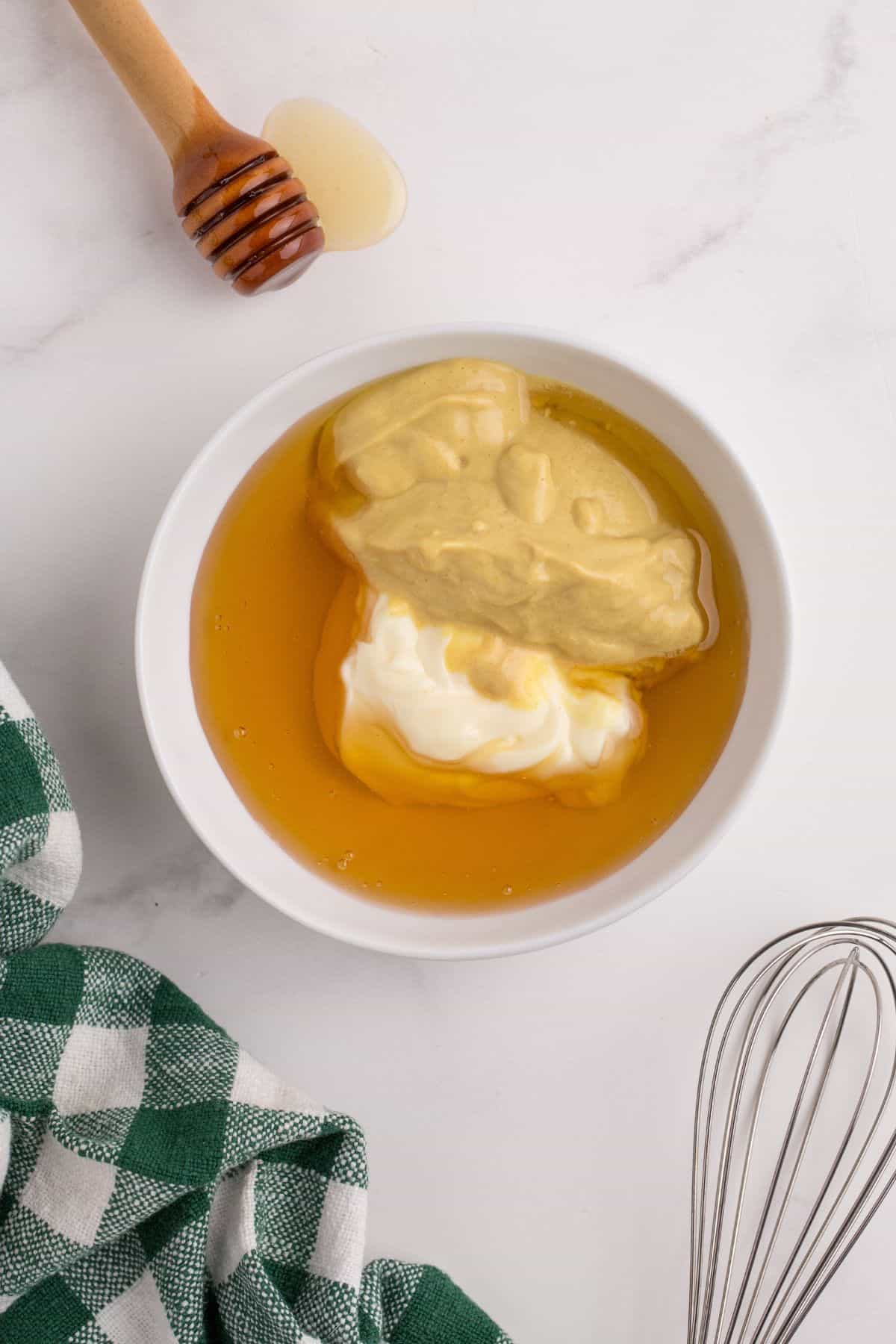 A small white bowl with measured amounts of honey, mayonnaise, and mustard.