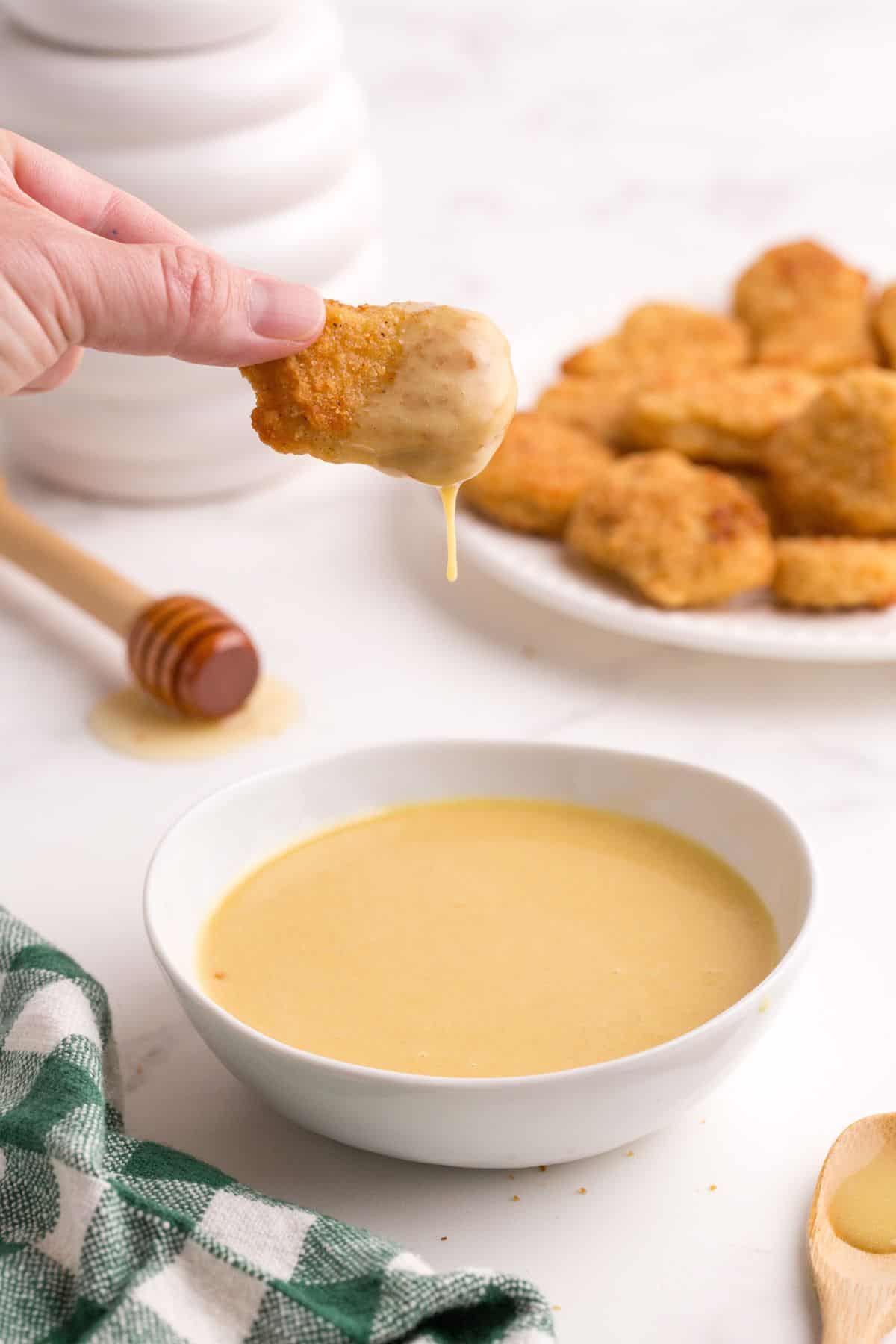 A chicken nugget is dunked into the bowl of honey mustard.
