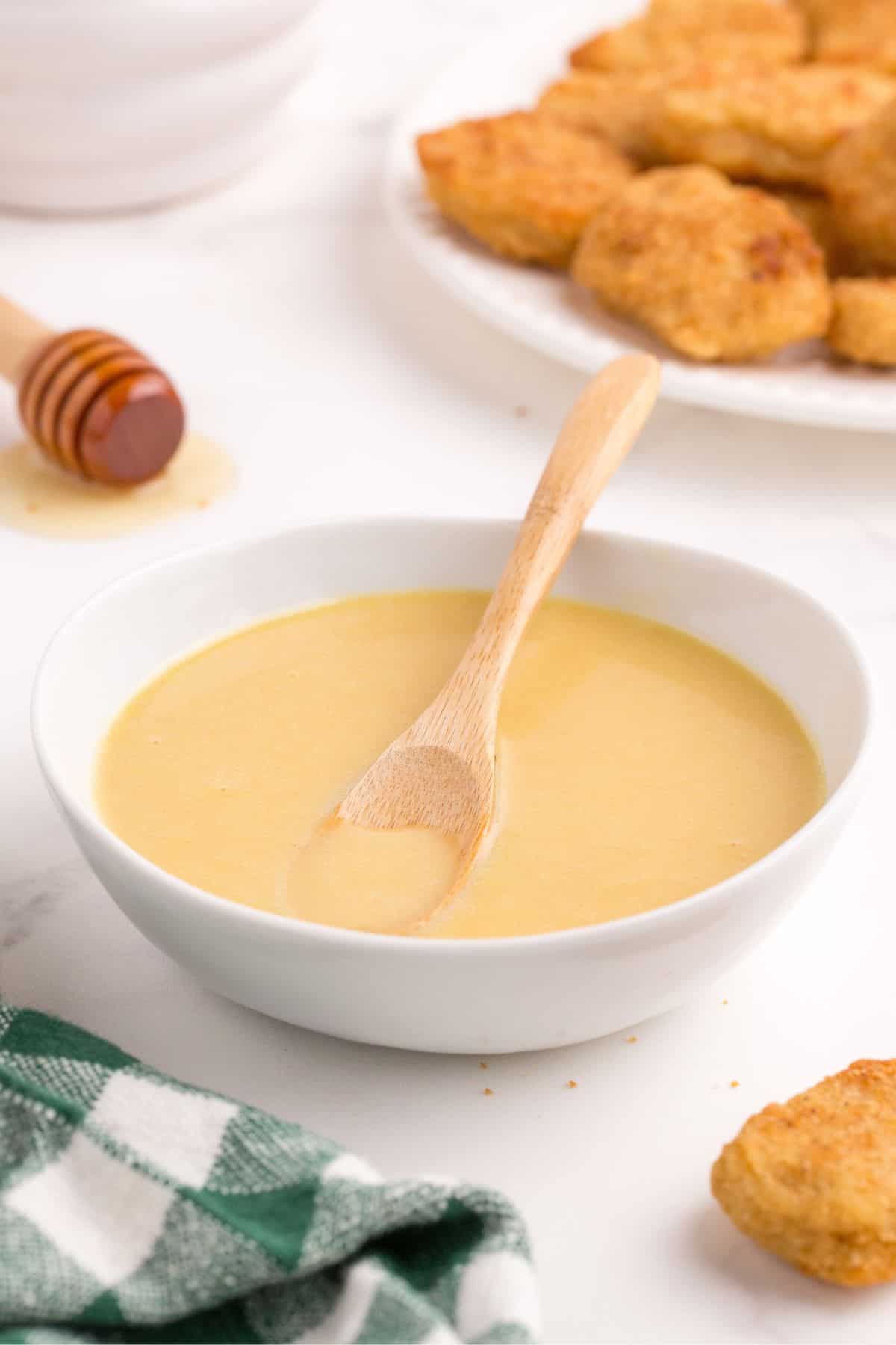 Small white bowl of honey mustard with a wooden spoon.