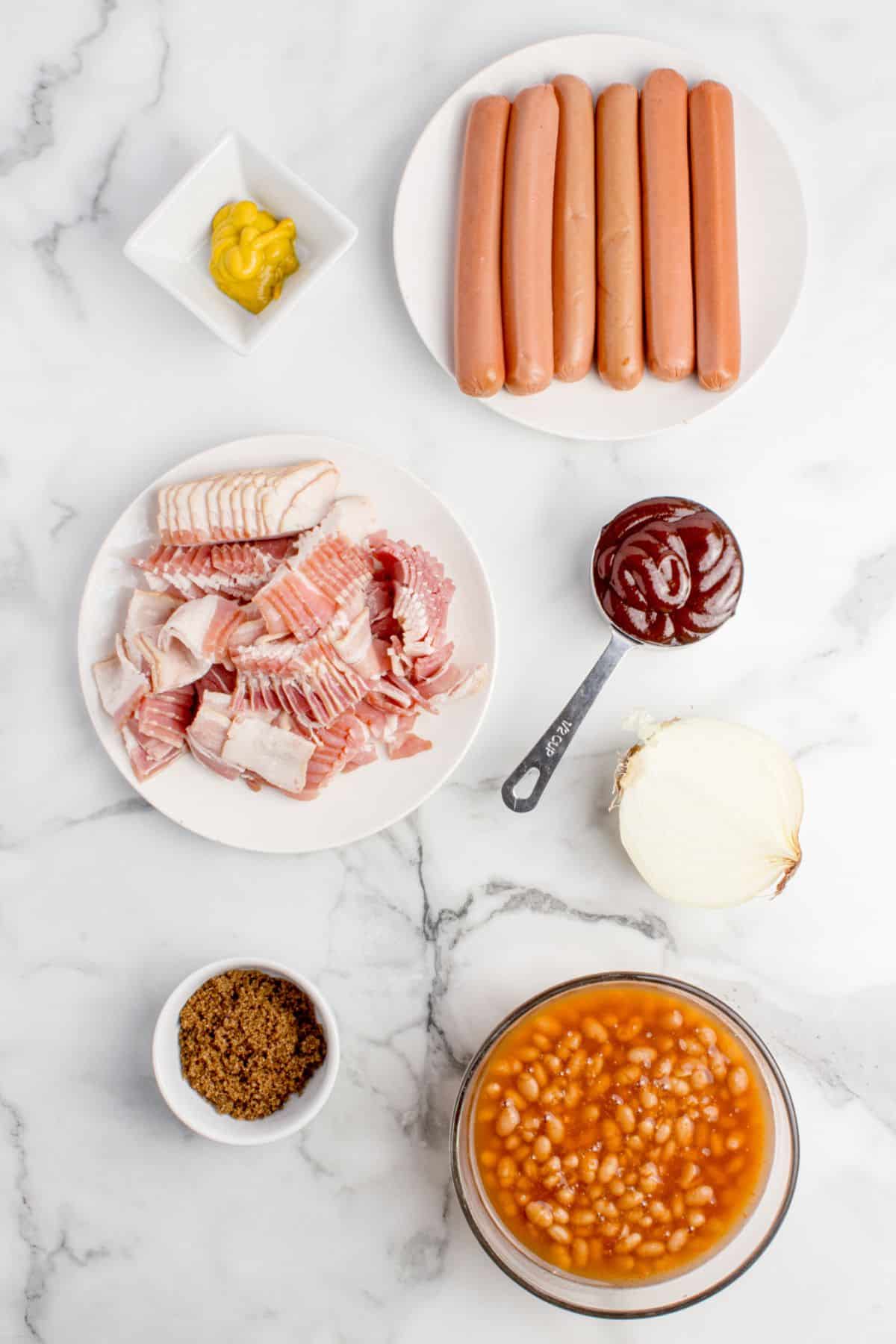 Ingredients for beanie weenies: mustard, hot dogs. bacon, BBQ sauce, onion, brown sugar, and canned beans.