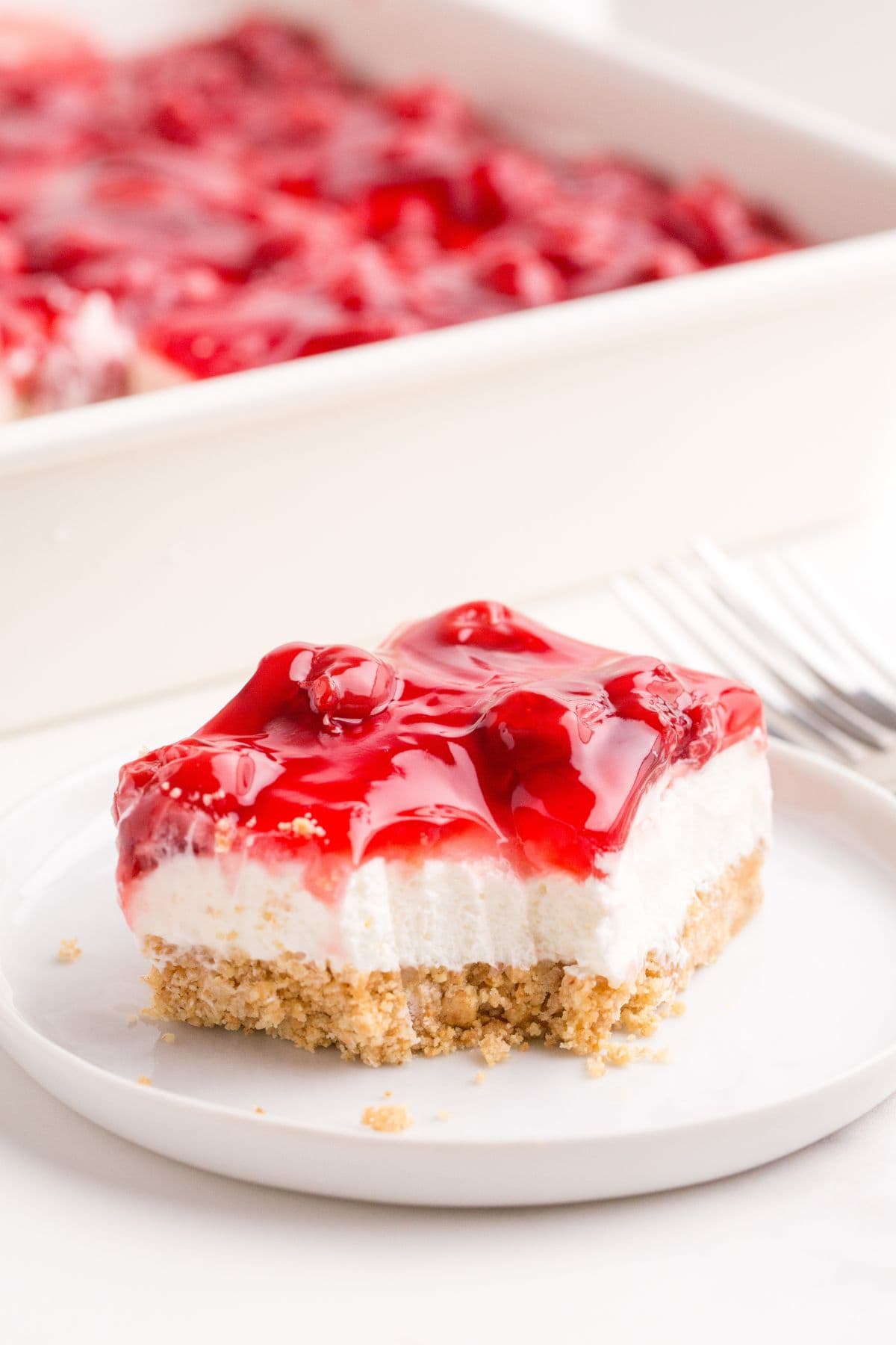 A slice of cherry delight on a white plate with a bite taken out of it.