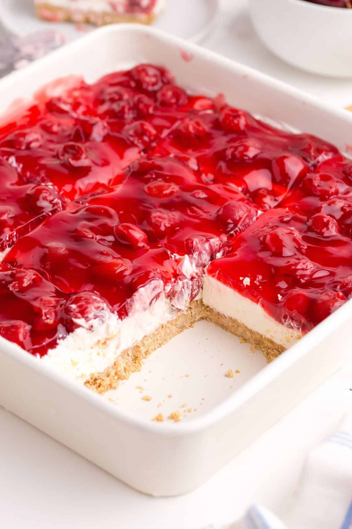 Cherry delight in a square white baking dish. Two slices have been removed to show the interior of the dessert.