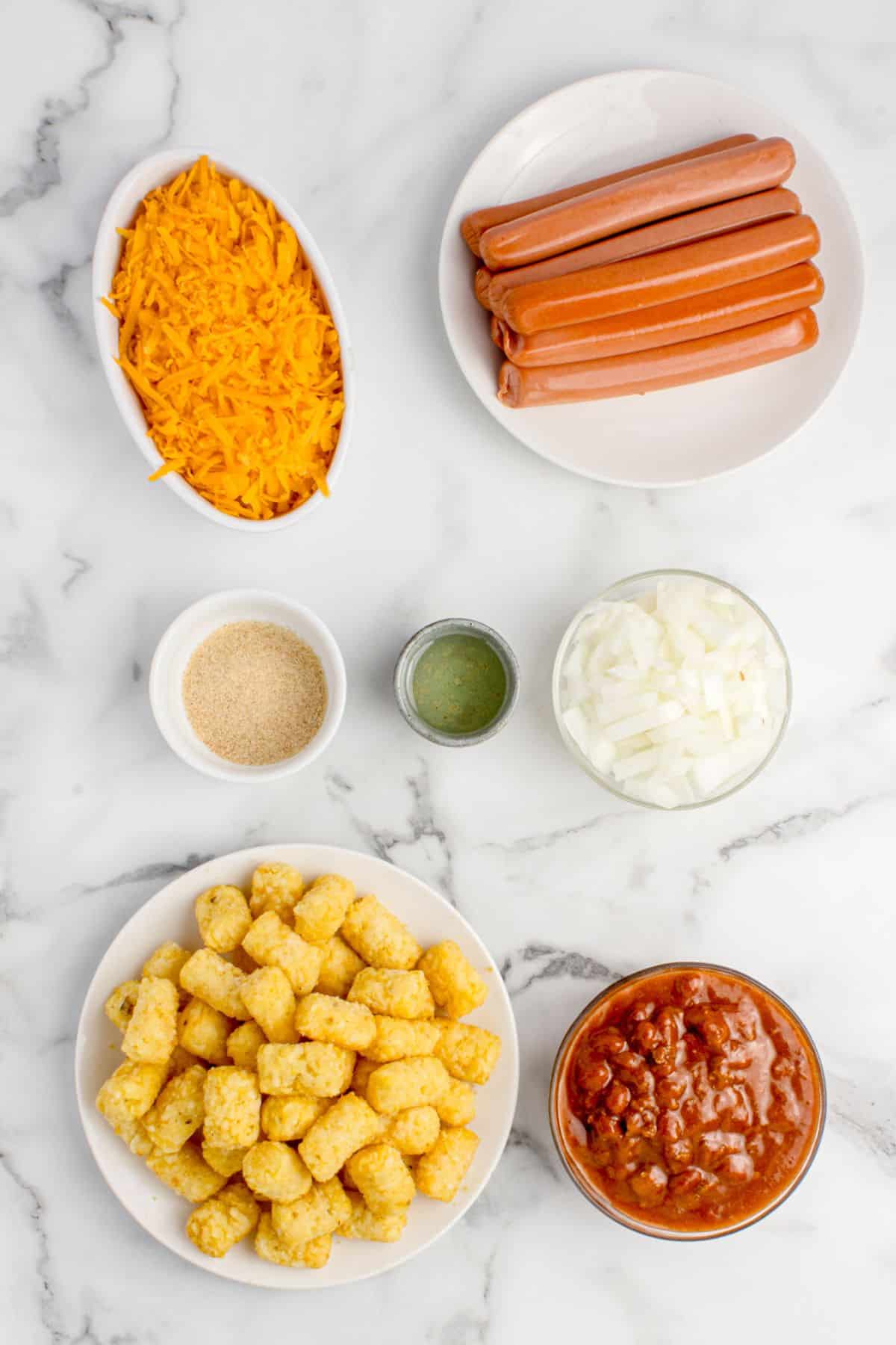 Ingredients for hot dog casserole: hot dogs, cheddar cheese, onion, oil, garlic powder, tater tots, and canned chili with beans.