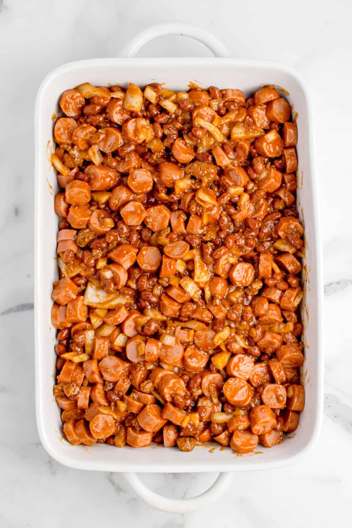 Onion, garlic powder, chili, and chopped hot dogs are combined at the bottom of the baking dish.
