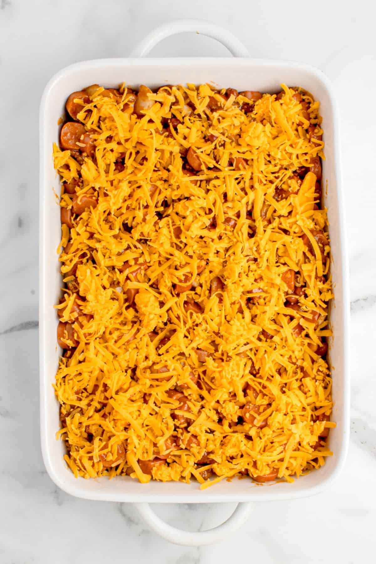 A layer of cheddar cheese is sprinkled over the top of the hot dog mixture.
