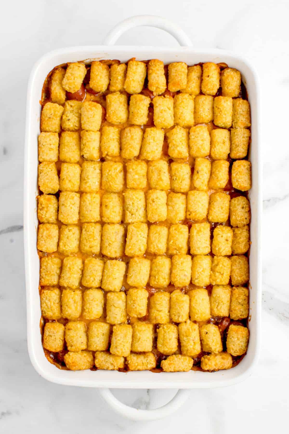 A single layer of tater tots are lined up on top of the cheese and hot dog mixture.
