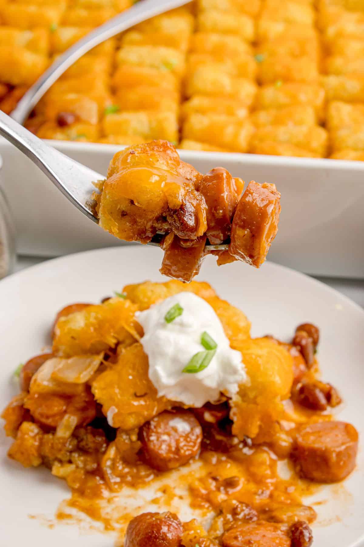 A fork lifting a bite of hot dog casserole off the white dinner plate.