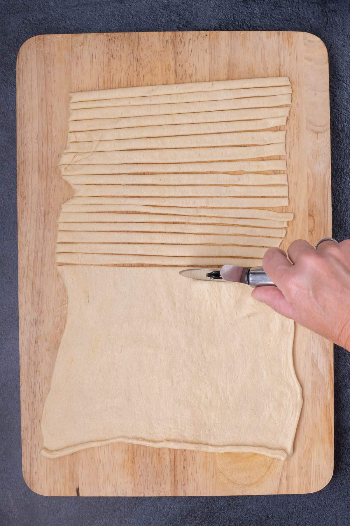 A pizza cutter is used to cut thin strips out of the crescent roll dough.