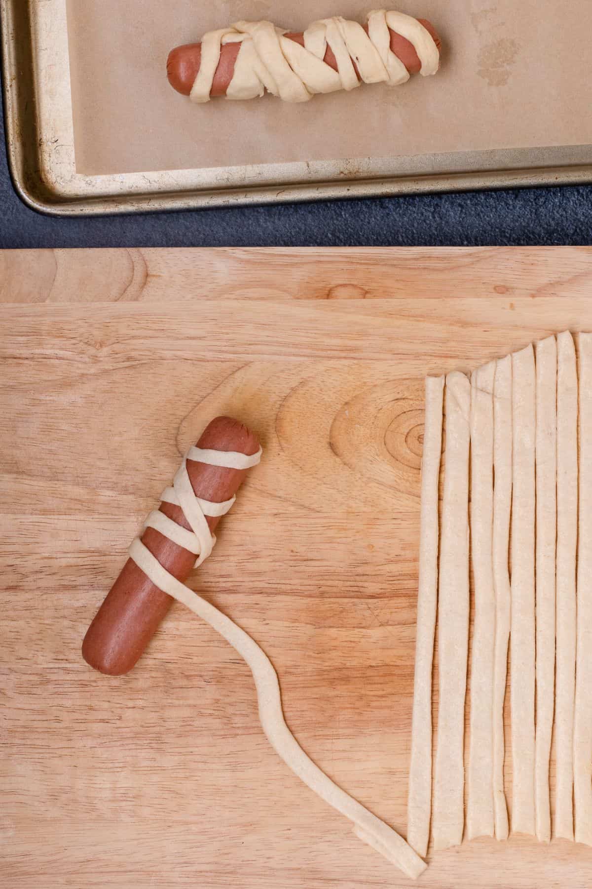 Strips of crescent rolls are rolled up around a hot dog to create a mummy look.
