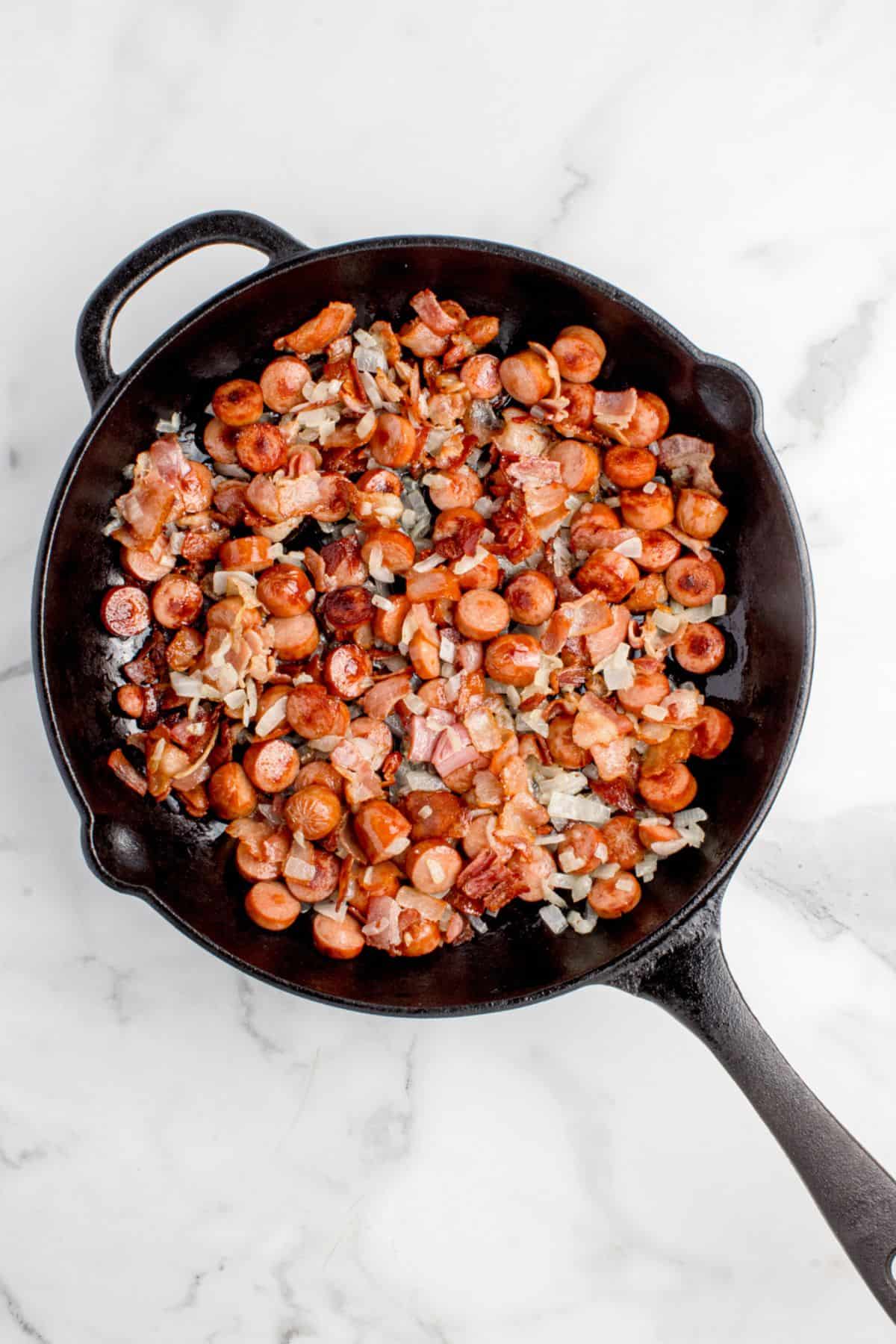The beanie weenies in a skillet with the onions sauteed.