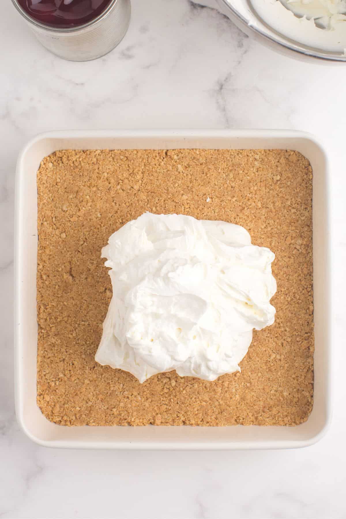 Cool whip and cream cheese topping being spread across the graham cracker crumb crust.