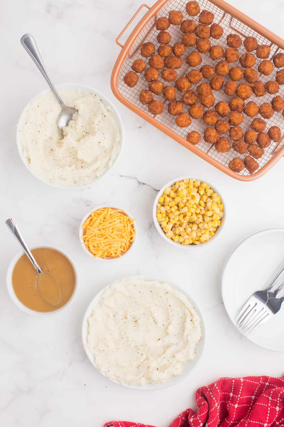 Ingredients needed to make a KFC chicken bowl: mashed potatoes, corn, popcorn chicken, gravy, and cheddar cheese.